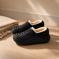 Waterproof indoor slippers in black on a pale oak floor